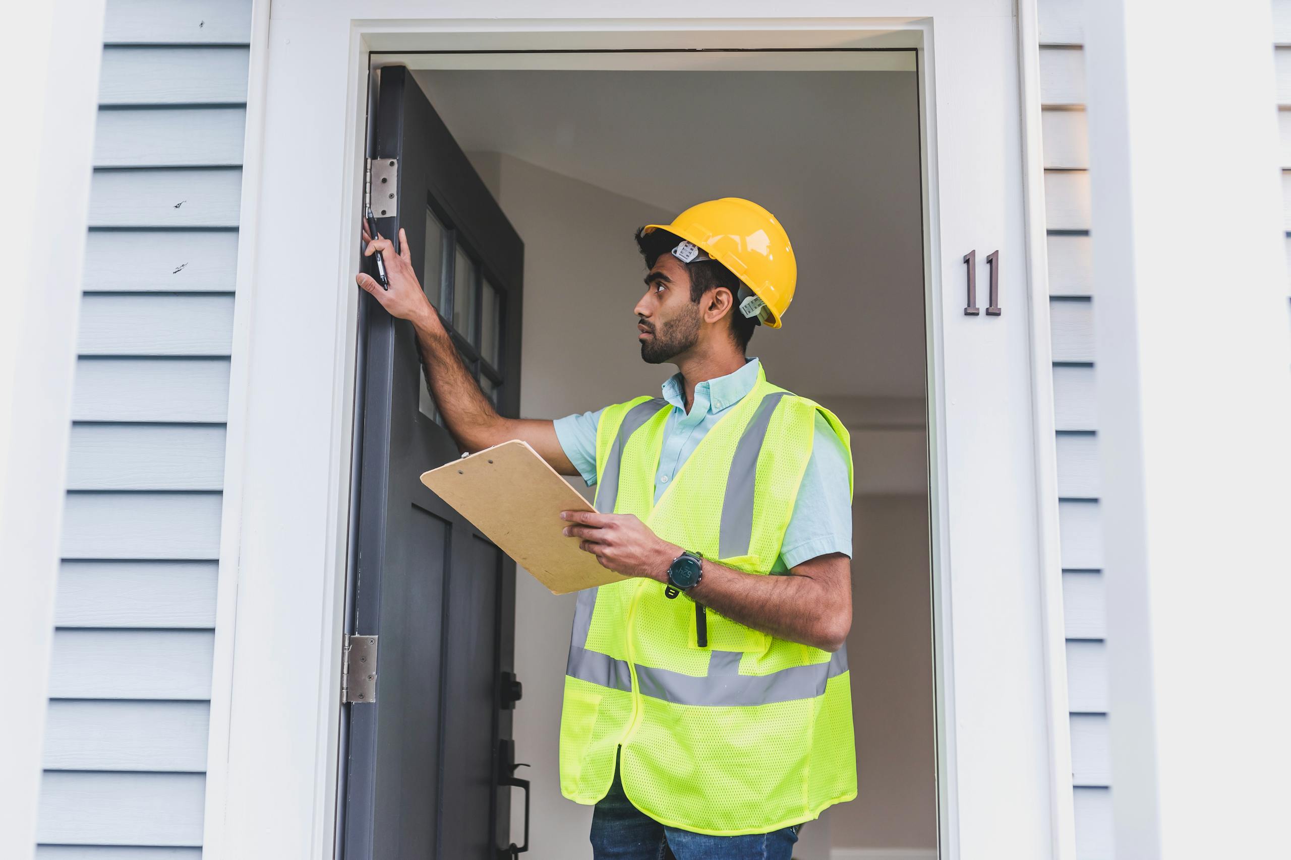 a home inspector in safety vest and hard hat checks doorframe alignment with clipboard outdoors 8293673 scaled